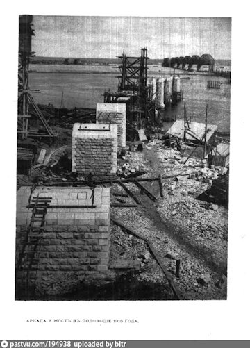 Az épülő híd az 1915-ös árvíz idején, kelet felől. Az átkelő elkészültét két nagyobb esemény késleltette. Először 1914. július 7-én hatalmas tűz ütött ki az építkezésen (a harmadik pillér állványzata összeomlott, megrongálva az elsőt és a másodikat is); másodszor – nem sokkal Roóbék átutazása után – a Szimbirszki-hegyi földcsuszamlás 1915. május 29-31-én nyolc hídpillért, a vasúti síneket és az állomást pusztított el vagy rongált meg; néhány pillért később töltéssel váltottak ki.